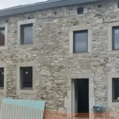 Façade d'une maison en pierre, en cours d'isolation. Fenêtres neuves et entrée ouverte sur un chantier.
