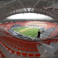 Pusta, nowoczesna arena stadionu Szachtara Donieck z pomarańczowymi i czarnymi siedzeniami oraz zieloną murawą.