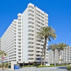 Edificio Sol con balcones curvos y palmeras bajo un cielo azul.