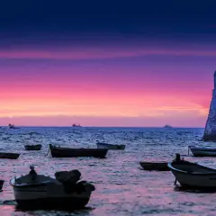 Barcas flotando en el mar al atardecer, con un castillo histórico y un cielo púrpura y rosa. Una hermosa puesta de sol en Cádiz.