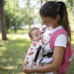 Uśmiechnięta mama z niemowlakiem w nosidełku z lisami. Fizjoterapeuta poleciłby takie, bo wspiera prawidłowy rozwój malucha.