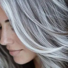 Perfil de mujer con cabello largo y ondulado, con un hermoso **grey blending** que combina tonos oscuros y plateados, creando un efecto natural y elegante.