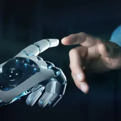 Dotyk ludzkiej dłoni i robota symbolizuje, jak powstała sztuczna inteligencja – połączenie ludzkiej kreatywności i technologii.