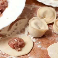 Przygotowanie pierogów z mięsem mielonym surowym. Na drewnianej desce leżą surowe pierogi, obok miska z farszem.