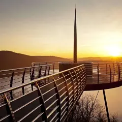 Ein Skywalk NRW bei Sonnenuntergang mit Blick auf einen See und bewaldete Hügel.
