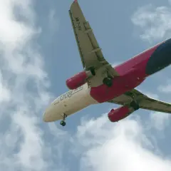 Samolot Wizz Air z wysuniętym podwoziem na tle nieba z chmurami.