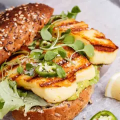 Un délicieux sandwich au halloumi grillé, garni de jalapeños et de jeunes pousses, prêt pour un barbecue estival.