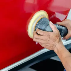 Ręce polerują czerwony lakier auta maszyną polerską. To kluczowy etap, jak woskować auto, by uzyskać lustrzany połysk i ochronę.