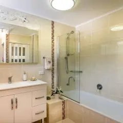 Baño moderno con ducha y bañera, lavabo con mueble y espejo decorado con un lagarto. El alicatar baño resalta con detalles en mosaico.