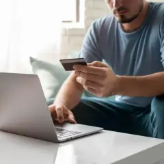 Mężczyzna z kartą płatniczą przed laptopem, uczy się, jak przelać pieniądze na PayPal z konta bankowego.