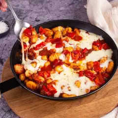 Gnocchis tomate mozza fondants, servis dans une poêle, avec une cuillère qui en prélève une portion filante.