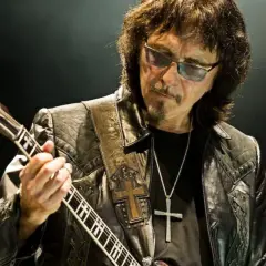 Tony Iommi fingers grają na gitarze, w okularach i skórzanej kurtce z krzyżem.