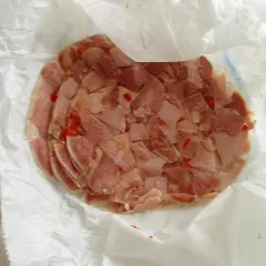 Rebanadas de queso de cabeza con trozos de pimiento rojo, envueltas en papel blanco.