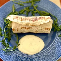 Ciepła tortilla z kurczakiem, podana z sosem i rukolą na niebieskim talerzu. Pyszne danie na szybki obiad.