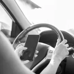 Une main tient un téléphone au volant, distrayant le conducteur. Une conduite dangereuse qui peut coûter 6 points sur le permis.