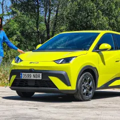 Mujer sonriente junto a un BYD Dolphin de vibrantes **colores** amarillos, destacando su diseño moderno en un entorno natural.