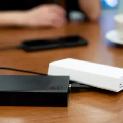 Dwa powerbanki, czarny i biały, leżą na drewnianym stole. W tle widać dłonie i filiżankę kawy. To idealny moment na sprawdzenie powerbank ranking.