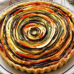 Quiche de verduras con hojaldre, un remolino de calabacín, berenjena y tomate sobre una base dorada.