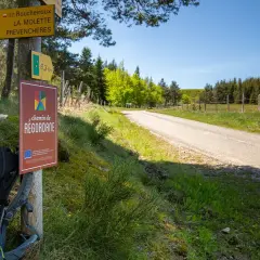Sac à dos prêt pour l'aventure sur le chemin de Regordane. Panneaux indicateurs et route s'étendent sous un ciel bleu.