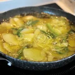 Patatas panaderas en sartén, dorándose en aceite caliente con cebolla y hierbas.