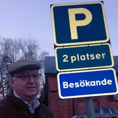 Man i keps vid parkering för personbil klass 2. Skylten visar "2 platser Besökande".