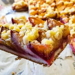 Ein Stück saftiger Zwetschgenkuchen auf Hefeteig mit Streuseln wird mit einer Gabel herausgehoben.