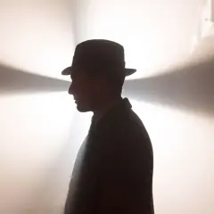 Ein Mann im Hut und Anzug, im Profil, vor einem hellen, strahlenden Hintergrund. Ein mysteriöser Blick, der an Babylon Berlin Staffel 5 erinnert.