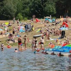 Tłum ludzi wypoczywa na plaży nad jeziorem Nakło Chechło. Woda jest spokojna, a na brzegu widać kolorowe rowerki wodne.