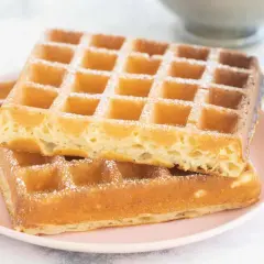 Zwei goldbraune belgische Waffeln, mit Puderzucker bestäubt, auf einem rosa Teller.