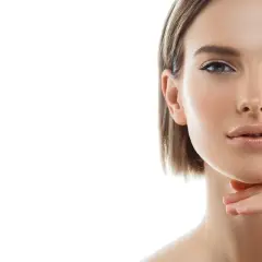 Primo piano di una donna con pelle luminosa e un tocco sul mento, un'ispirazione per chi cerca come snellire il viso con un look naturale.