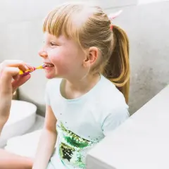 Uśmiechnięta dziewczynka z piegami cieszy się porannym szczotkowaniem zębów.
