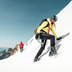 Wspinaczka po śnieżnym zboczu z asekuracją lotną. Dwoje alpinistów w kaskach i sprzęcie pokonuje górę.