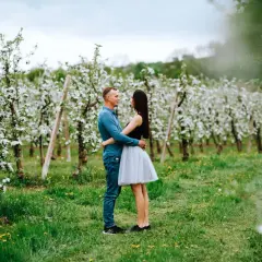 Para zakochanych przytula się w kwitnącym sadzie. Ich sesja wiosenna w otoczeniu białych kwiatów jabłoni to piękny obraz miłości.