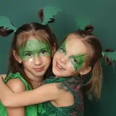 Zwei Mädchen mit Drachenschminke und grünen Flügeln im Haar, ein einfaches Drachen-Kinderschminken-Ergebnis.