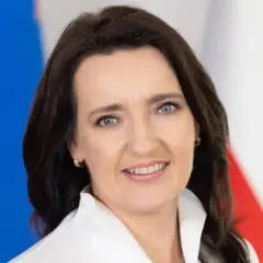 Marzena Okła-Drałowicz, uśmiechnięta kobieta z ciemnymi włosami, na tle biało-czerwonej flagi.