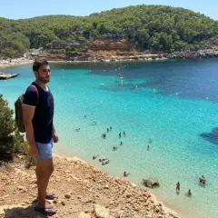 Un hombre con mochila admira una cala turquesa en Ibiza. ¡Un plan perfecto que ver en Ibiza en 4 días!