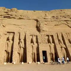 Gigantescas estatuas talladas en la roca flanquean la entrada del templo de Abu Simbel. Turistas admiran la majestuosidad de este sitio histórico.