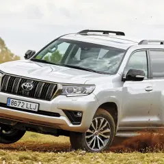 Un Toyota KDJ 120 plateado derrapa en un camino de tierra, levantando barro.