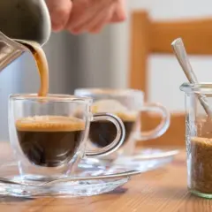 Frisch gebrühter Kaffee wird in ein Glas gegossen. Ob Kaffee den Blutdruck beeinflusst, ist eine häufige Frage. Daneben steht Zucker.