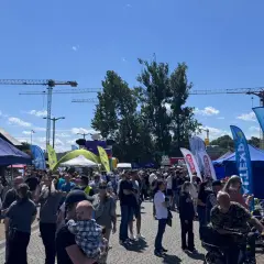 Tłum ludzi na zewnątrz, namioty, flagi i dźwigi w tle.