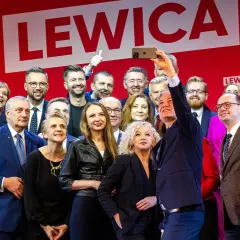 Grupa polityków Lewicy pozuje do selfie na tle czerwonej ściany z logo partii.