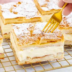 Ein goldener Löffel sticht in ein Stück polnischer Puddingkuchen, bestäubt mit Puderzucker.