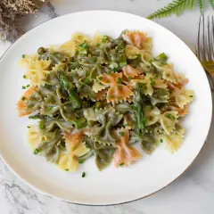Plato de pasta primavera con farfalle tricolor, espárragos y guisantes en salsa cremosa, adornado con cebollino picado.