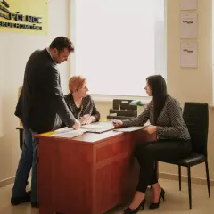 Trzy osoby przy biurku w biurze, dyskutujące nad dokumentami.