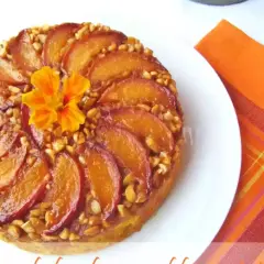 Deliziosa torta di pesche rovesciata, con pesche caramellate, noci croccanti e un fiore arancione al centro.