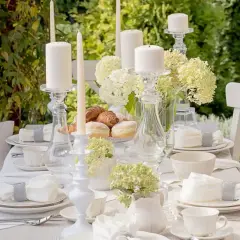Elegancki stół na rocznicę komunii w ogrodzie. Białe świece, kwiaty i słodkości tworzą magiczną atmosferę.