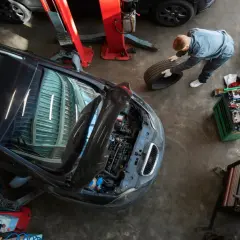 Mechanik w warsztacie samochodowym trzyma oponę obok podniesionego samochodu i skrzynki z narzędziami.