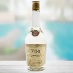 Butelka Feni, indyjskiego alkoholu z nerkowców, na tle basenu.