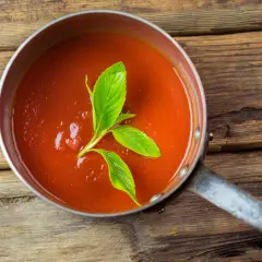 Frische, hausgemachte tomatensauce aus reifen Tomaten, garniert mit Basilikum, in einem Topf auf rustikalem Holz.