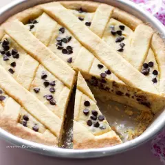 Deliziosa crostata ricotta e gocce di cioccolato, con una fetta tagliata per mostrare il ripieno cremoso e le gocce scure.